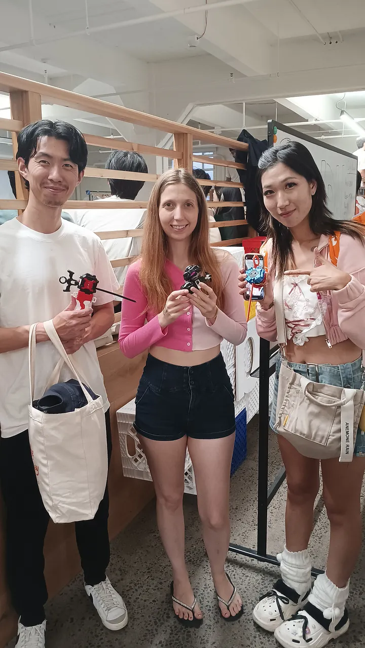 Three people stand together smiling, holding Beyblades and launchers that they modified for the competition.
