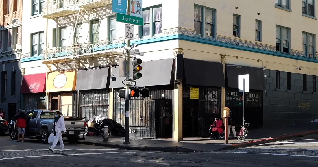 A daytime shot of a city street corner, showing the intersection of Jones and Ellis, with a cream-colored building, dark awnings, and people on the sidewalk.