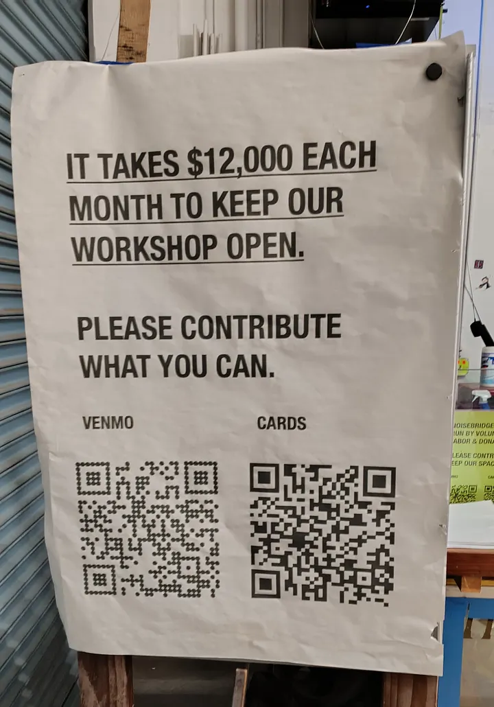 A white paper sign requests donations, stating "IT TAKES $12,000 EACH MONTH TO KEEP OUR WORKSHOP OPEN," and provides QR codes for Venmo and cards.